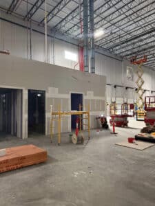 the inside of an amazon fulfillment center under construction with various construction lifts and a lightgauge co worker working on a wall