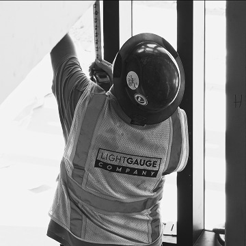 lightgauge co worker wearing a hard hat and reaching up to measure something on the construction site