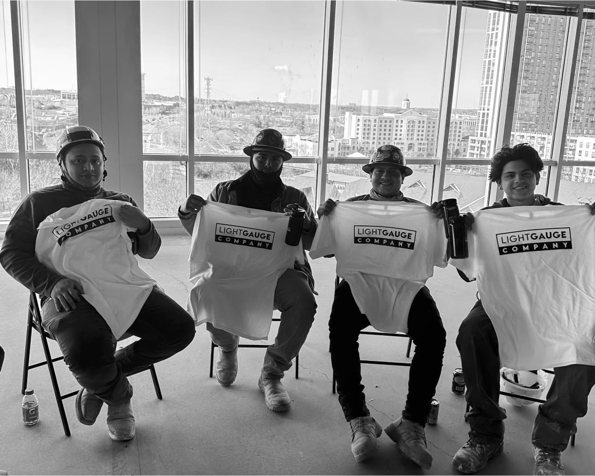 four lightgauge co workers sitting down onsite holding up lightgauge co shirts while wearing hard hats